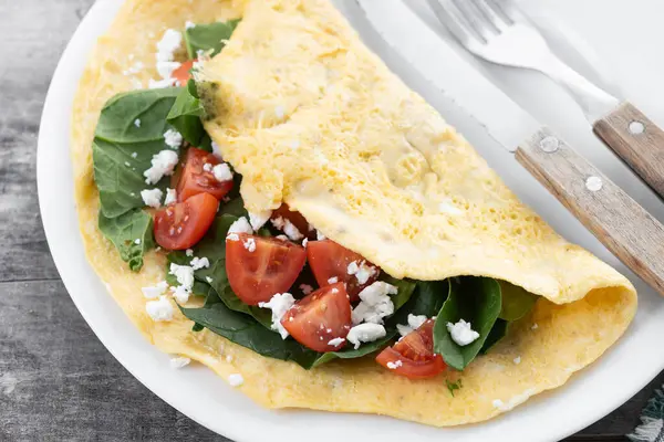 Domatesli omlet ve ahşap masada ıspanak.