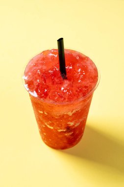 Sarı arka planda kırmızı çilekli içecek.