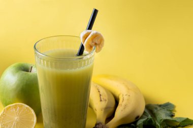 Sarı arka planda ıspanaklı, muzlu, elmalı ve limonlu yeşil smoothie.
