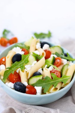 İçinde al dente makarna, kiraz domatesleri, salatalık, zeytin, kırmızı soğan ve taze bitkiler bulunan canlı Akdeniz makarna salatası. Zeytinyağı ve limon suyuyla karıştırılmış.