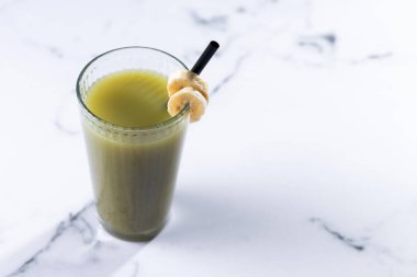 Beyaz mermer üzerinde ıspanaklı, muzlu, elmalı ve limonlu yeşil smoothie. Boşluğu kopyala