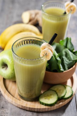Tahta masalarda ıspanaklı, muzlu, elmalı ve limonlu yeşil smoothie.