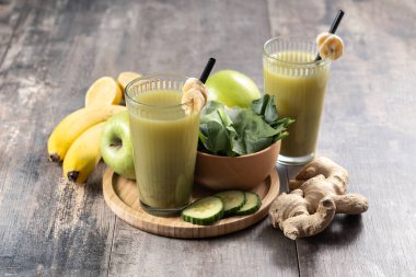 Ahşap masa üzerinde ıspanaklı, muzlu, elmalı ve limonlu yeşil smoothie.
