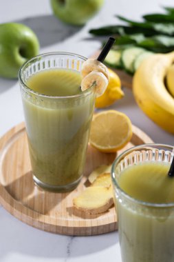 Beyaz mermer üzerinde ıspanaklı, muzlu, elmalı ve limonlu yeşil smoothie.