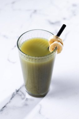 Beyaz mermer üzerinde ıspanaklı, muzlu, elmalı ve limonlu yeşil smoothie.