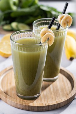 Beyaz mermer üzerinde ıspanaklı, muzlu, elmalı ve limonlu yeşil smoothie.