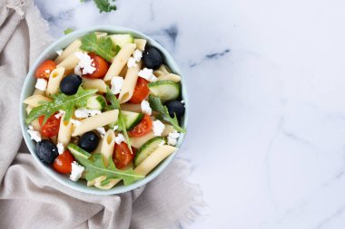 Akdeniz makarna salatası kasede taze sebzeler ve beyaz mermer üzerinde bitkiler. Üst Manzara. Boşluğu kopyala