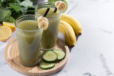 Beyaz mermer üzerinde ıspanaklı, muzlu, elmalı ve limonlu yeşil smoothie. Boşluğu kopyala