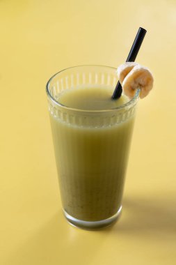 Sarı arka planda ıspanaklı, muzlu, elmalı ve limonlu yeşil smoothie.