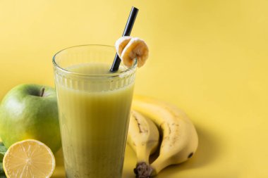 Sarı arka planda ıspanaklı, muzlu, elmalı ve limonlu yeşil smoothie. Boşluğu kopyala