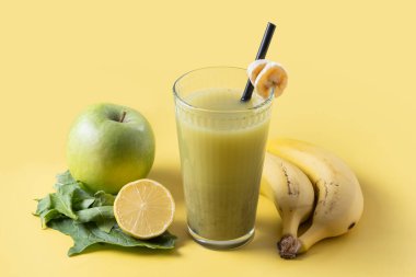 Sarı arka planda ıspanaklı, muzlu, elmalı ve limonlu yeşil smoothie.
