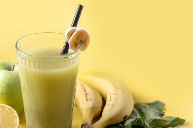 Sarı arka planda ıspanaklı, muzlu, elmalı ve limonlu yeşil smoothie.