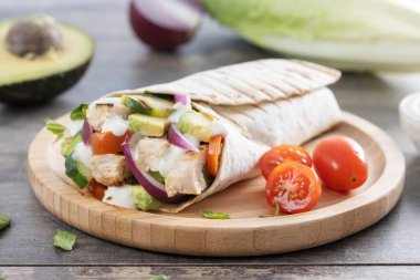 Lezzetli ızgara tavuk dürümü, sebzeli ve ahşap masada avokado.