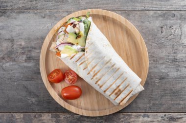 Lezzetli ızgara tavuk dürümü, sebzeli ve ahşap masada avokado.