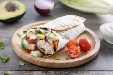 Lezzetli ızgara tavuk dürümü, sebzeli ve ahşap masada avokado.