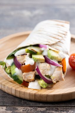 Lezzetli ızgara tavuk dürümü, sebzeli ve ahşap masada avokado.