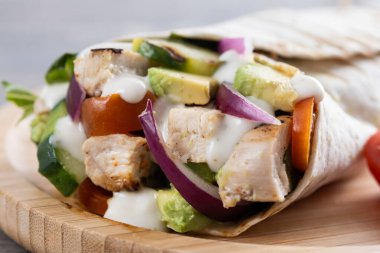 Lezzetli ızgara tavuk dürümü, sebzeli ve ahşap masada avokado.