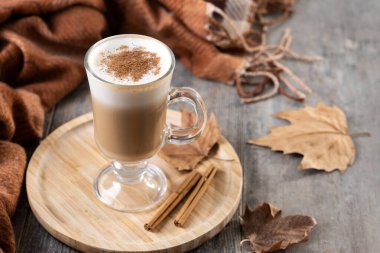 Tarçın tozuyla kaplanmış ılık akçaağaç latte, ahşap tepside cam bardakta servis ediliyor. Boşluğu kopyala