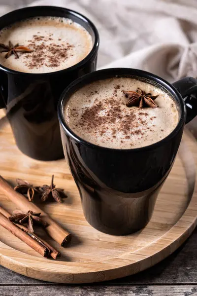 Kara bardakta Chai Latte ve Baharatlar (yıldız anason ve tarçın) ahşap masa üzerinde