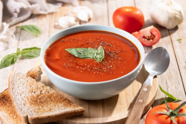 Ev yapımı domates çorbası ve ahşap masada fesleğen.