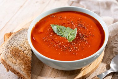 Ev yapımı domates çorbası ve ahşap masada fesleğen.