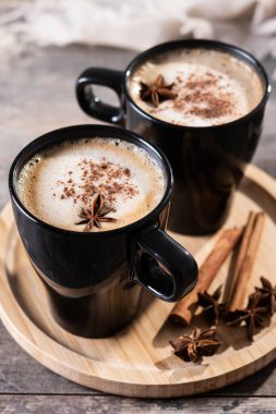 Kara bardakta Chai Latte ve Baharatlar (yıldız anason ve tarçın) ahşap masa üzerinde