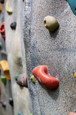 Renkli tırmanışların yakın çekim görüntüsü yapay bir kaya duvarını tutuyor..