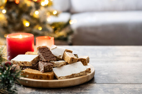 Ассорти традиционной новогодней нуги на деревянной тарелке со свечами на заднем плане. Копирование пространства