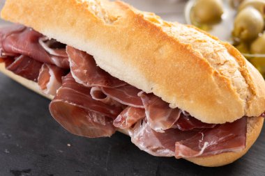 Ahşap masaya konmuş ekmek ekmeğinden yapılmış lezzetli bir Serrano jambonlu sandviç.