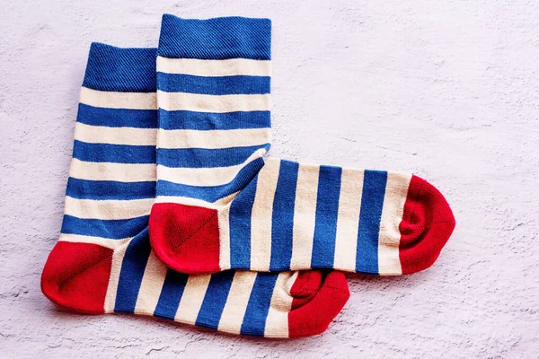 Blue and beige striped socks with a red toe and heel. A pair of socks on a gray cement background.