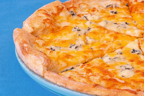 Mavi tabakta peynirli pizza. Mavi masa örtüsü üzerinde dört peynirli pizza.