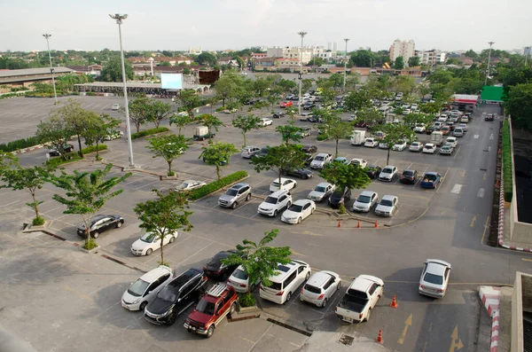 A lot of car parking in outdoor parking lot,Many tree plant and grow in car park, yellow direction arrow on the street.