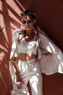 Saçları örgülü, beyaz takım elbiseli, egzotik çiçekleri ve gölgeleri olan şık bir kadın..