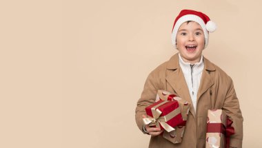 Noel hediyeleriyle ve açık kahverengi arka planda şok olmuş yüzüyle komik küçük çocuk..