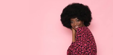 Güzel esmer, afro saçlı, kırmızı çiçekli elbisesi ve soyutlanmış pembe arka planı var..