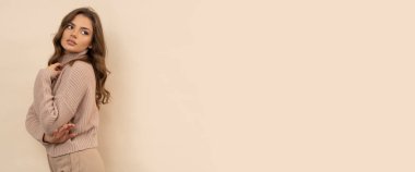 Kahverengi arka planda kahverengi kazaklı çekici genç bir kadının stüdyo fotoğrafı..