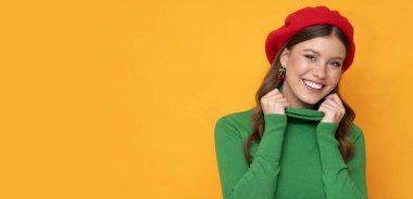 Very attractive young woman with awesome smile weared in red beret and green golf on orange background.