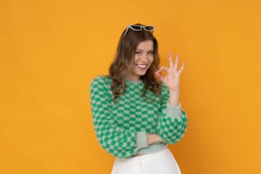 Gorgeous young woman with pretty smile in green sweater on orange background.