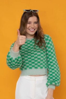 Gorgeous young woman with pretty smile in green sweater on orange background.