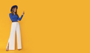 Happy woman with blue hat and elegant clothes on isolated orange background.