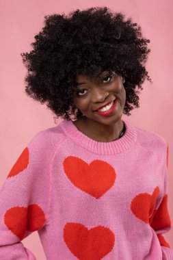 Pembe arka planda kalp süveteri giyen güzel Afrikalı kadın..