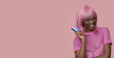 Pembe saçlı ve pembe arka planda kredi kartı olan mutlu bir model..