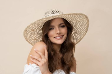 Very attractive brunette in straw hat and white dress on creamy background.