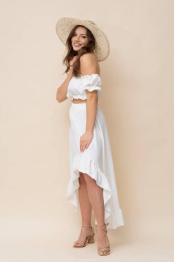 Very attractive brunette in straw hat and white dress on creamy background.