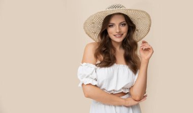 Very attractive brunette in straw hat and white dress on creamy background.