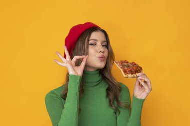 İzole edilmiş turuncu arka planda pizza yiyen güzel bir kadın..