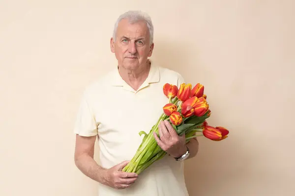 スタジオでクリームの背景にチューリップの花束を持つハンサムなシニアマン — ストック写真