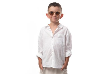 Muslin gömlekli, bej pantolonlu ve beyaz arka planda deri sandaletli yakışıklı bir çocuk. Modaya uygun modern görünüş!