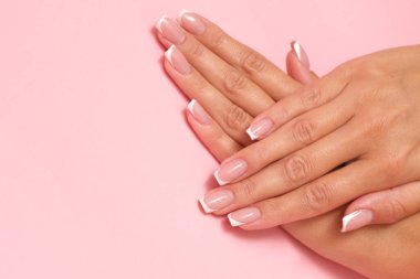 Pastel pembe arka planda Fransız manikürlü güzel kadınsı eller..