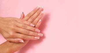 Pastel pembe arka planda Fransız manikürlü güzel kadınsı eller..